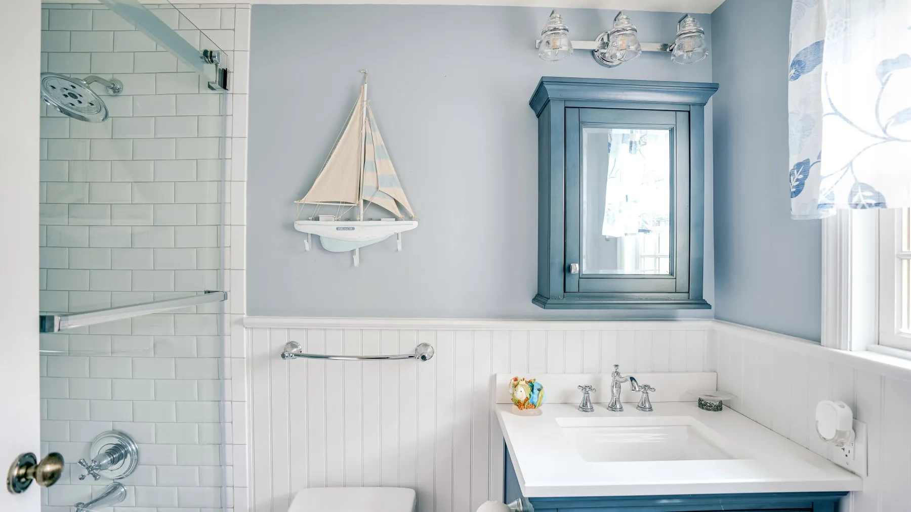 A bathroom with a glass shower, a vanity, and a decorative sailboat.