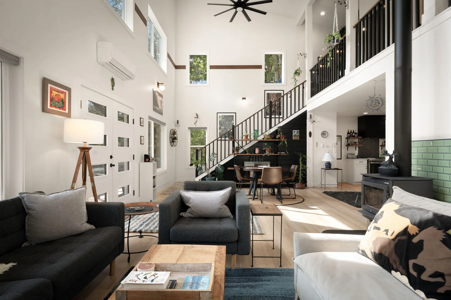 Una luminosa sala de estar de planta abierta, con asientos bajo una escalera y un balcón interior.
