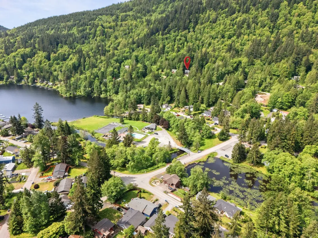 Vista aérea de casas y caminos junto a un lago y colinas boscosas.