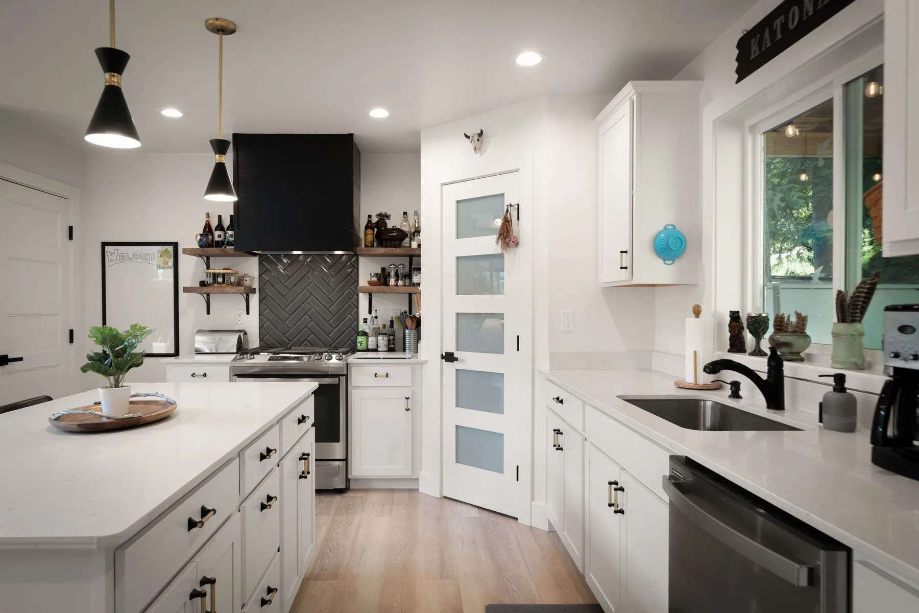 Una cocina blanca y luminosa con isla, salpicadero oscuro y electrodomésticos de acero inoxidable.