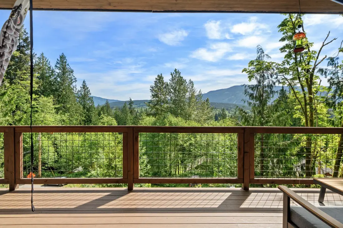 Una terraza de madera da a un bosque verde y montañas lejanas.