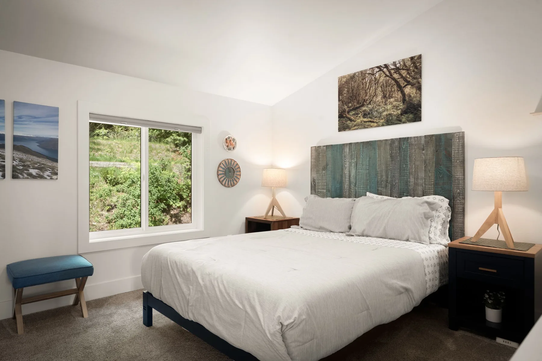 Un dormitorio luminoso con una cama tendida y una ventana grande con vistas a la vegetación.