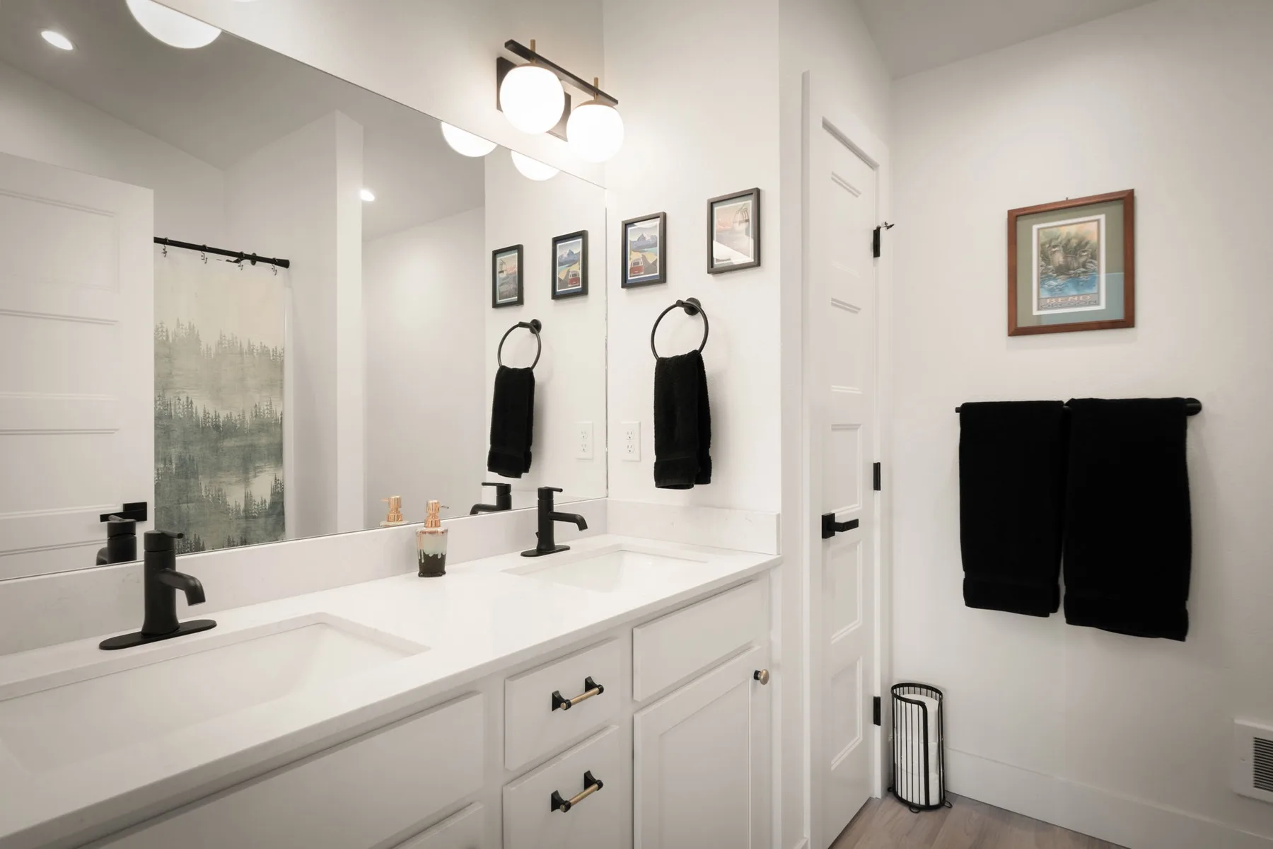 Un tocador de baño luminoso con un espejo amplio y toallas negras colgadas en la pared.