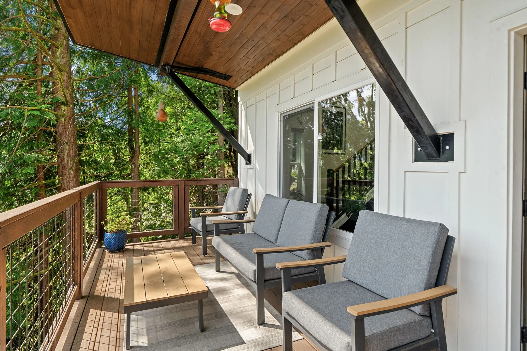 Una terraza exterior cubierta con asientos y una mesa de centro de madera da a árboles frondosos.