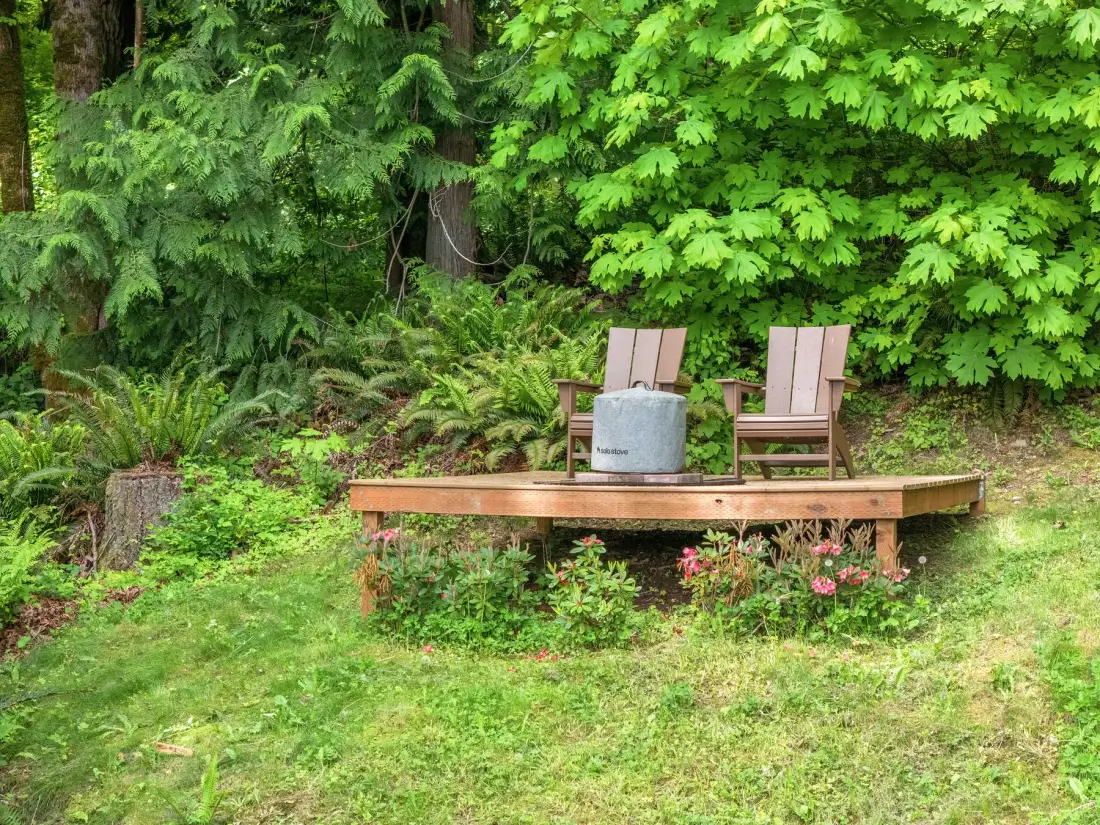 Una plataforma de madera con dos sillas está rodeada de vegetación.