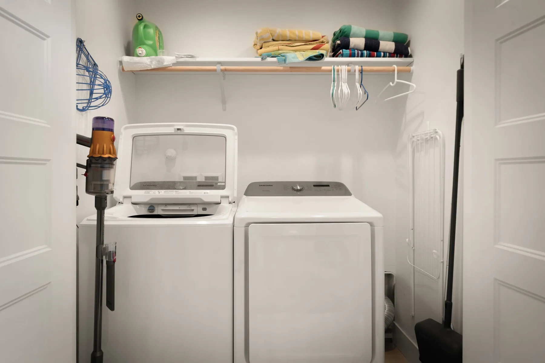 Un cuarto de lavado con lavadora y secadora debajo de un estante con toallas dobladas.