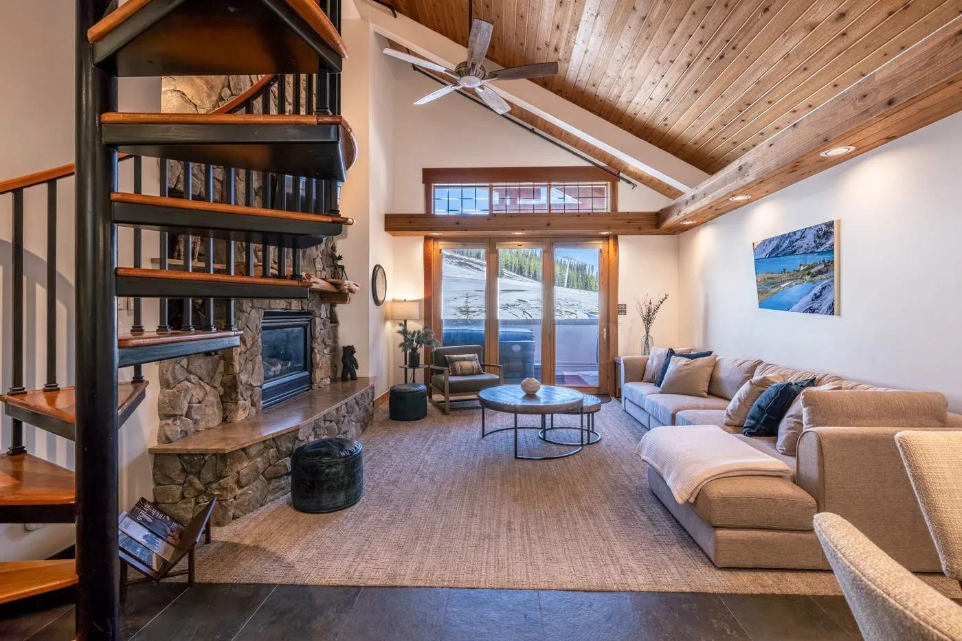 A living room with a stone fireplace, seating, and a high wood-paneled ceiling.
