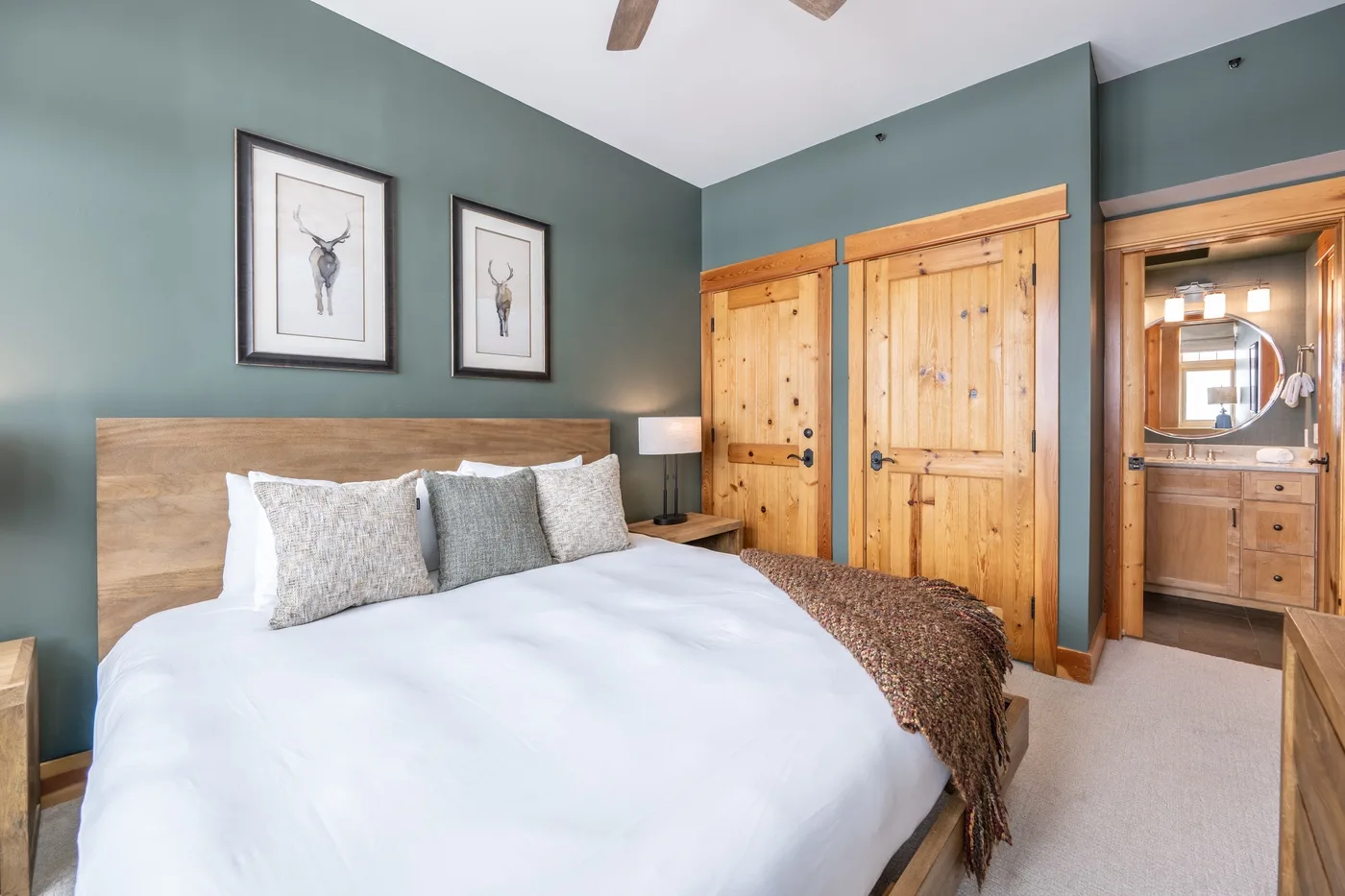 A bedroom with a bed, framed artwork, and wooden doors opening to a bathroom.