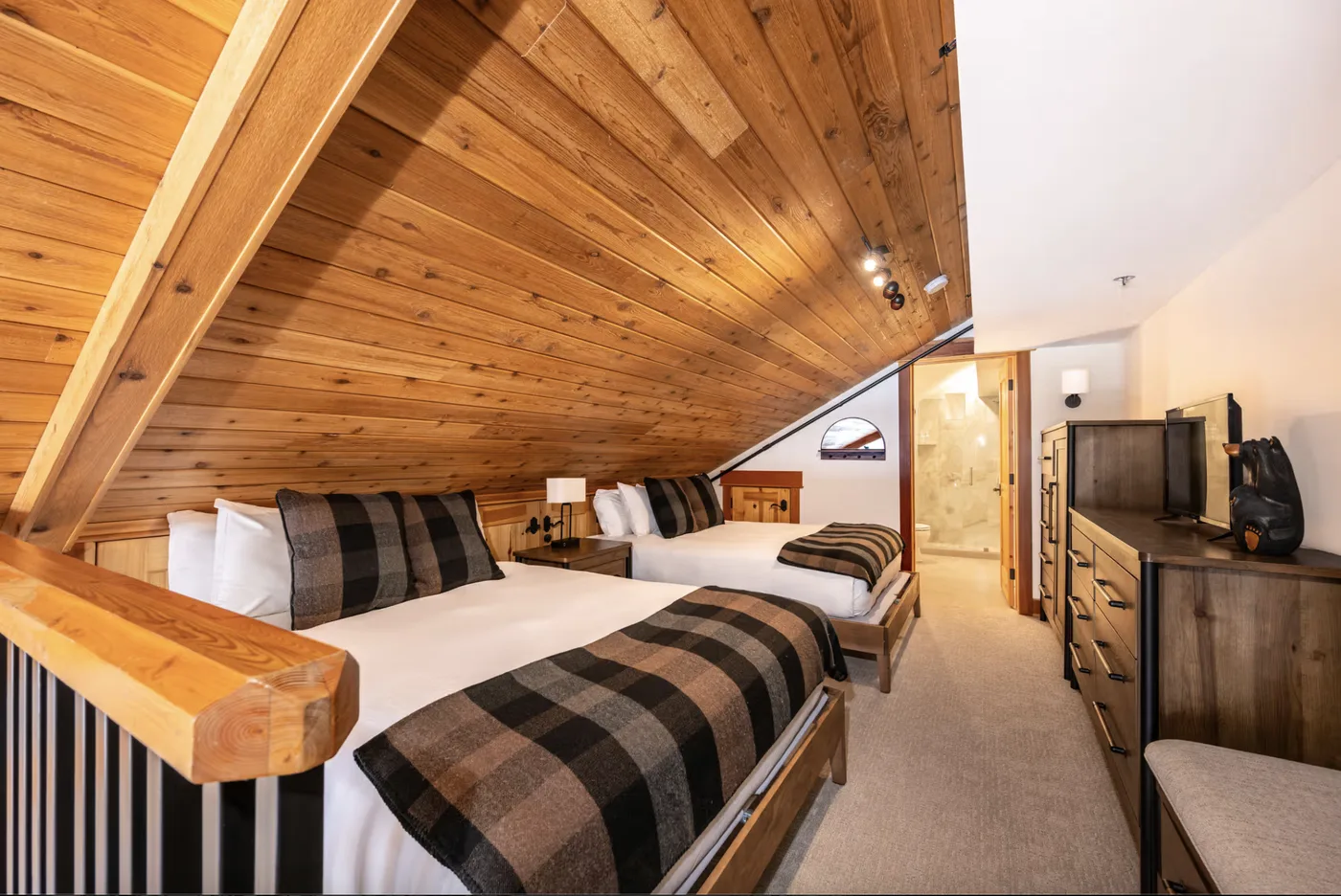 A bedroom with two beds beneath a sloped wooden ceiling.