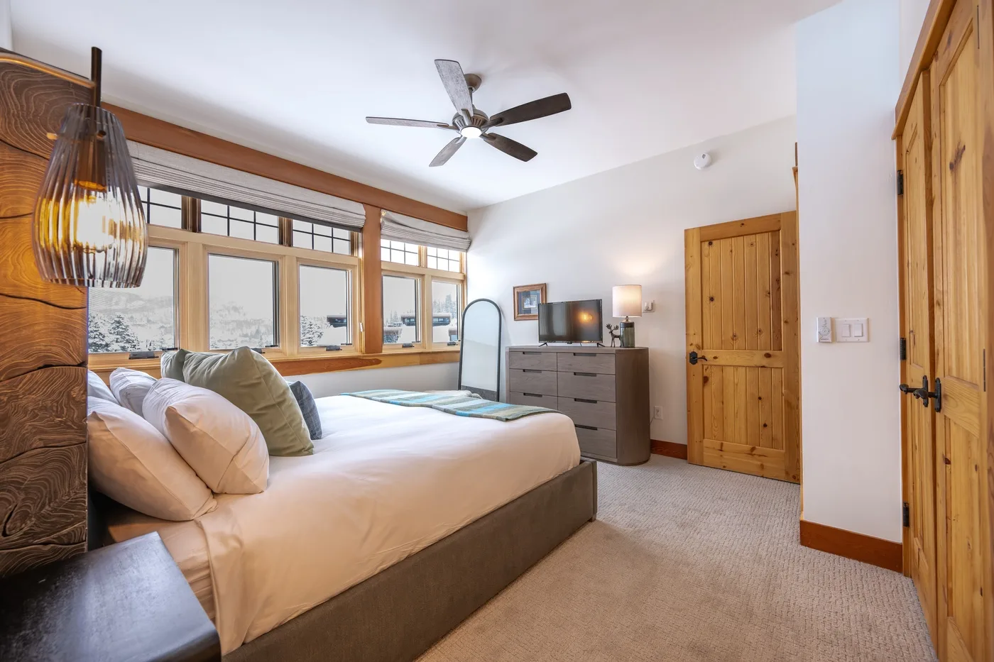 A bedroom with a large bed, wood-framed windows, and a dresser.