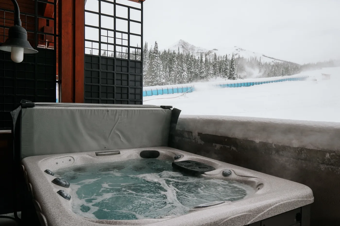 An outdoor hot tub sits beside a snowy landscape and a wooded ridge.