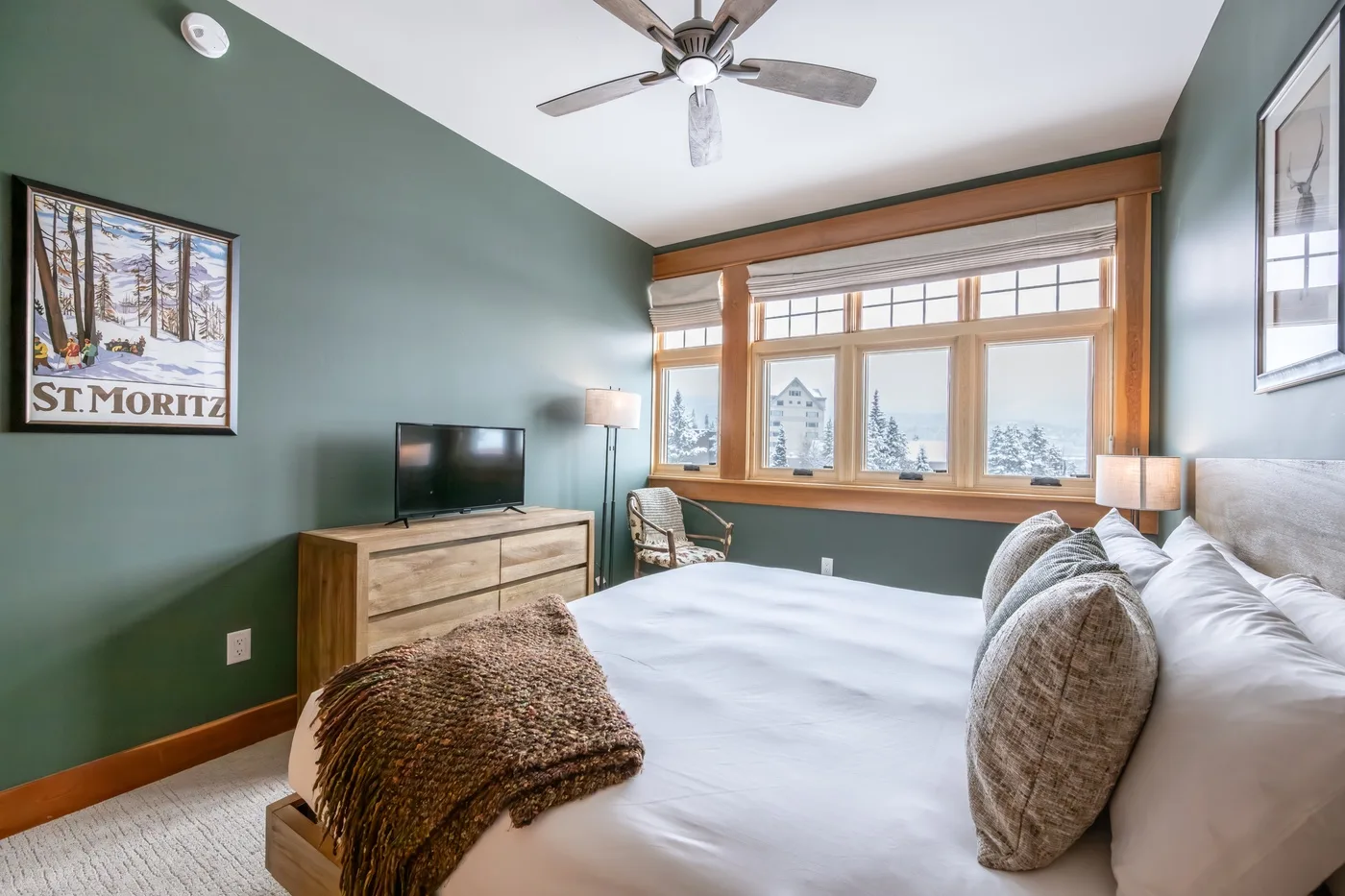 A bedroom with a large bed, green walls, and windows overlooking snowy trees.