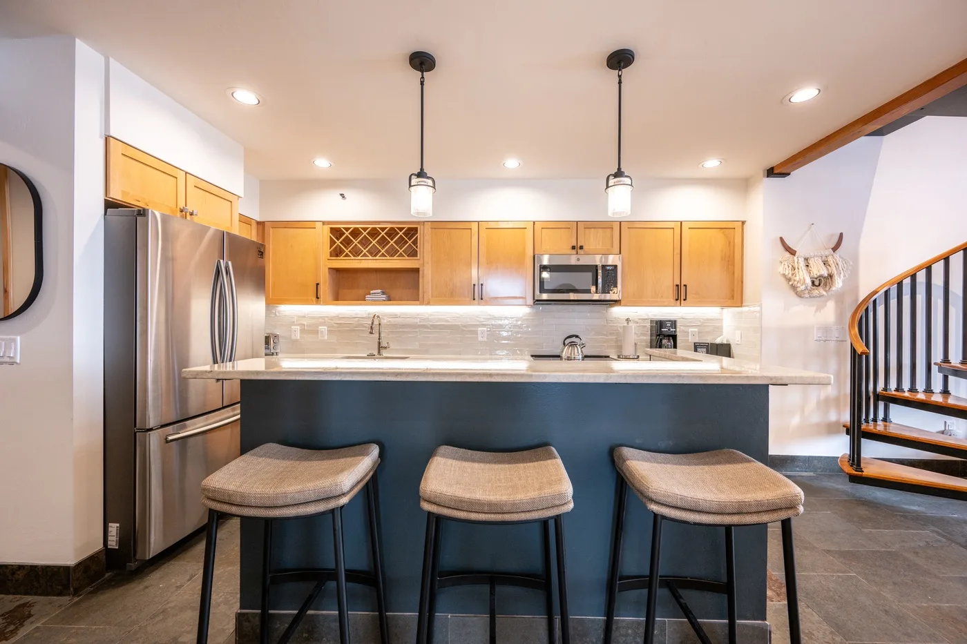A bright kitchen with a wide island and three stools.