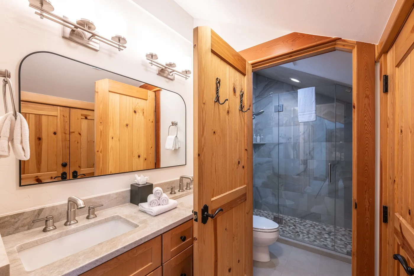 A bathroom vanity with a sink and mirror beside an open doorway to a tiled shower.