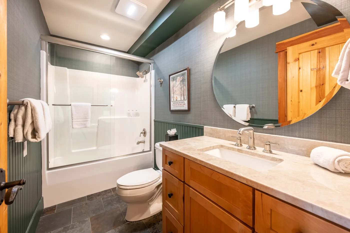 A bathroom with a bathtub-shower, toilet, and wooden vanity.