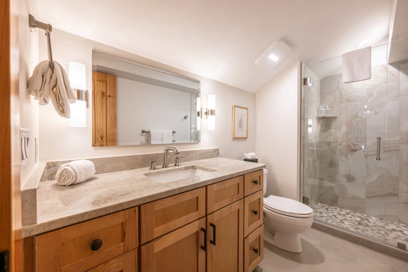 A bathroom vanity with a wide mirror, toilet, and glass shower.