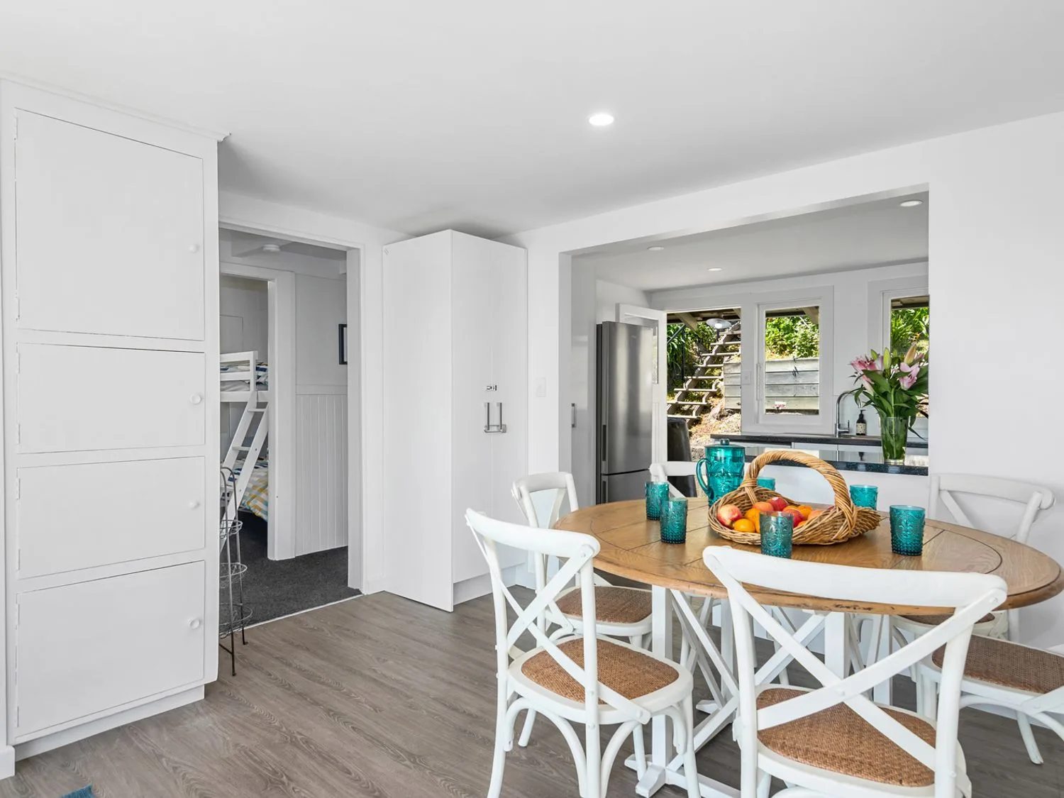 A dining area with a round table, white seating, and a fruit basket.