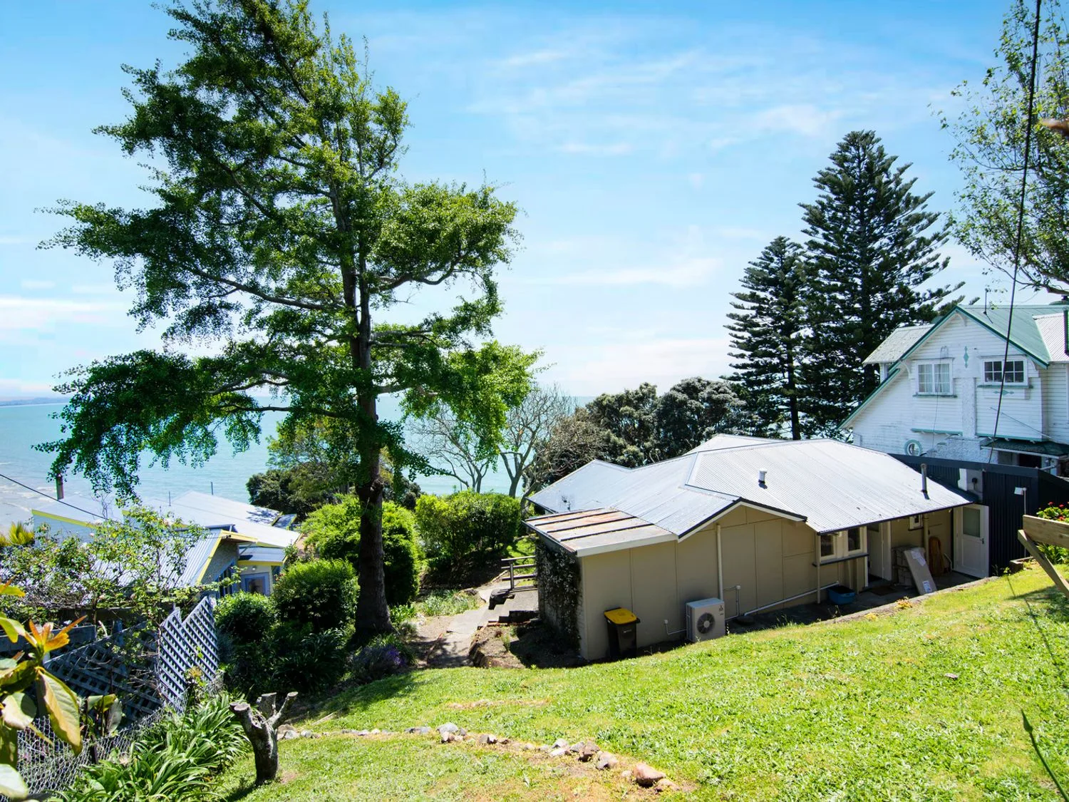 Una vista de una ladera con casas, árboles y el mar al fondo en Bayview Bungalow Nelson.