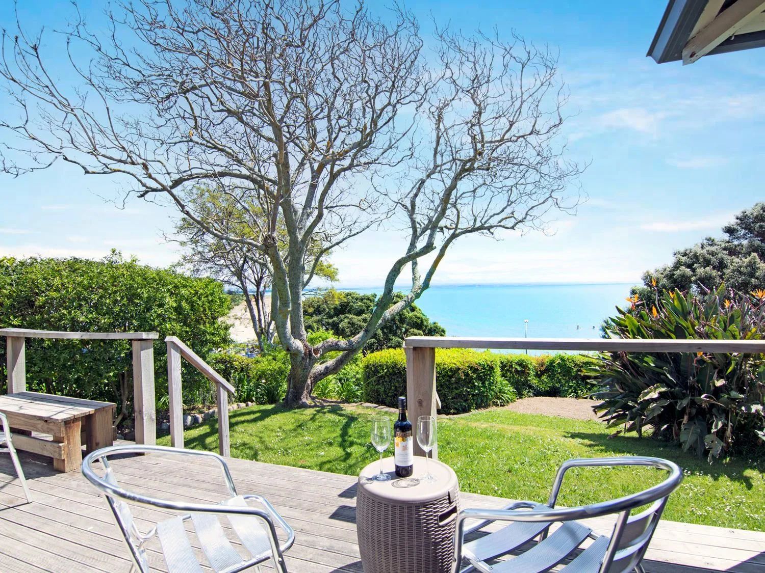 A wooden deck with outdoor seating overlooks a grassy yard and the ocean.