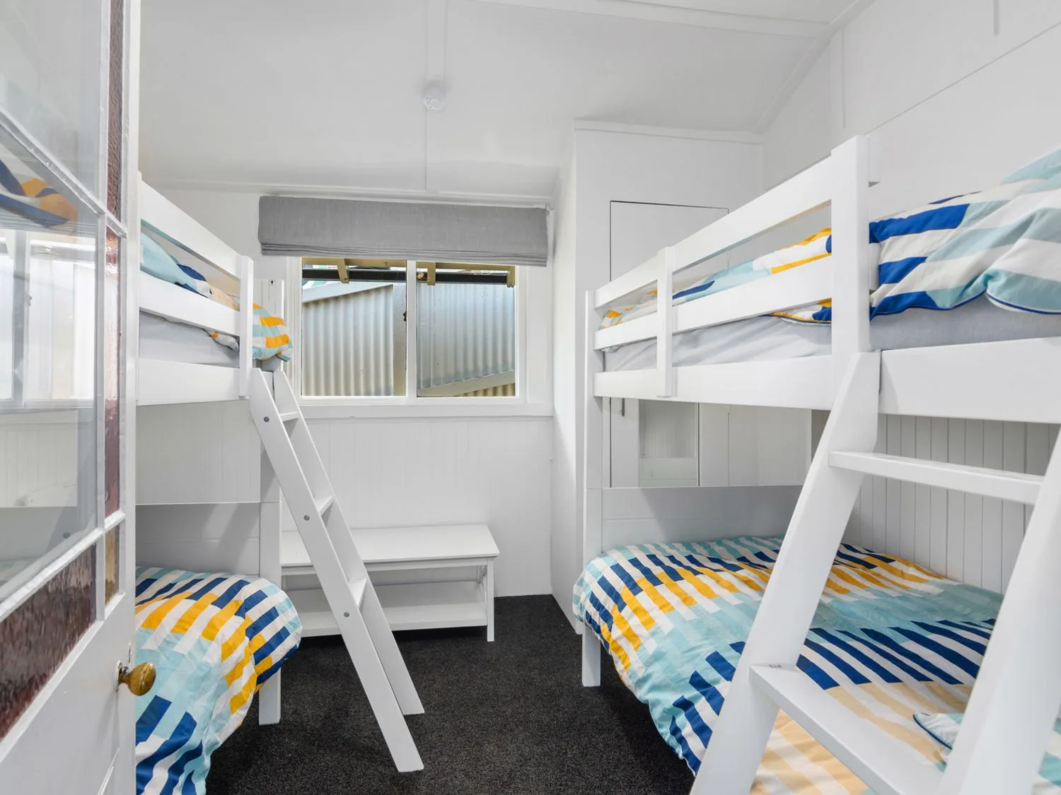 Un dormitorio con dos literas blancas y una mesa pequeña debajo de una ventana en Bayview Bungalow - Nelson Holiday Home, en Nelson.