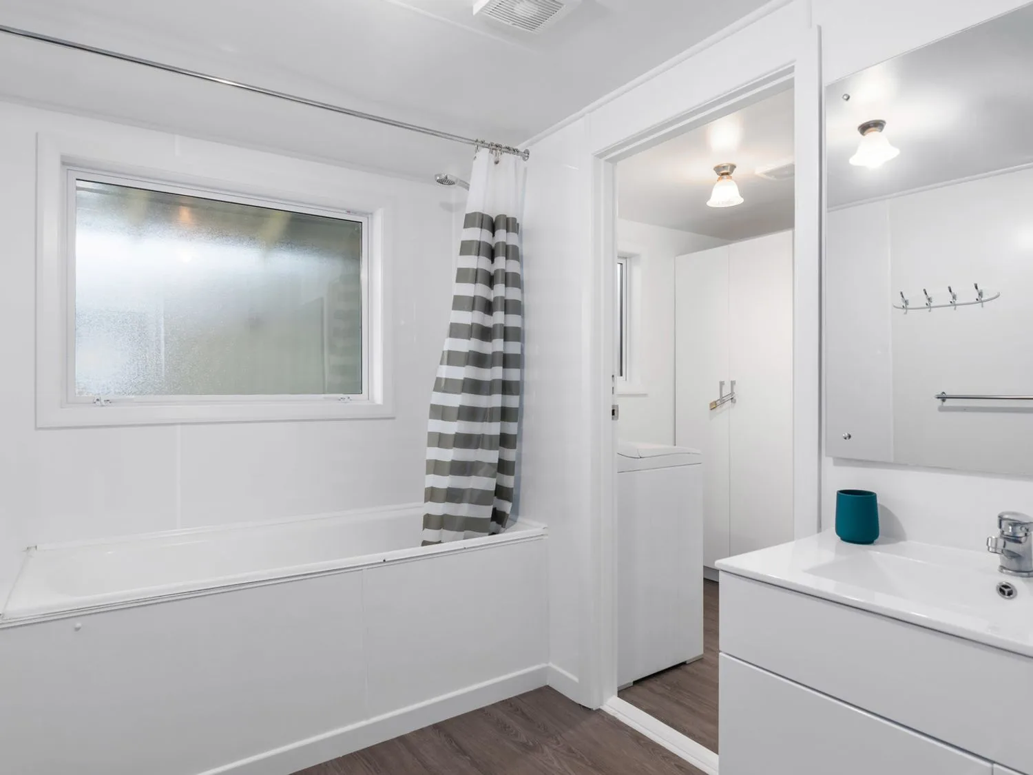 Un baño con bañera, cortina de ducha a rayas y lavabo junto a una puerta abierta.
