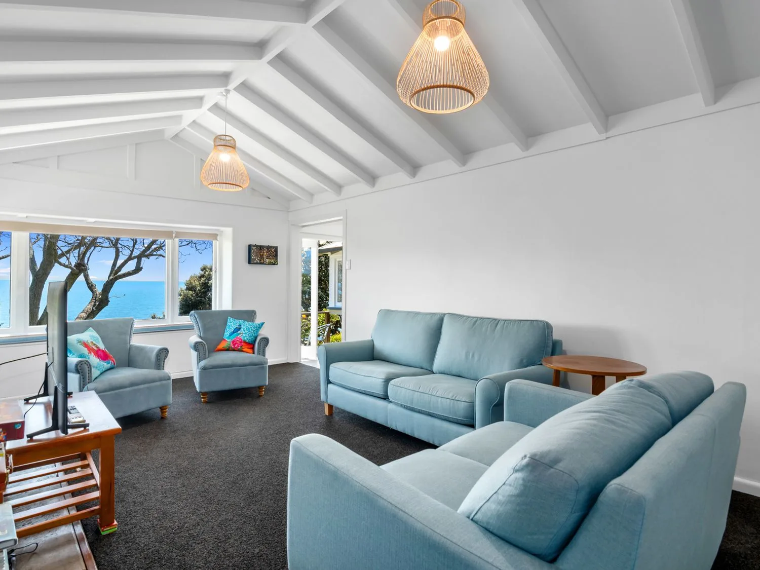 Una sala de estar con asientos azules, un televisor y una ventana con vistas al mar.