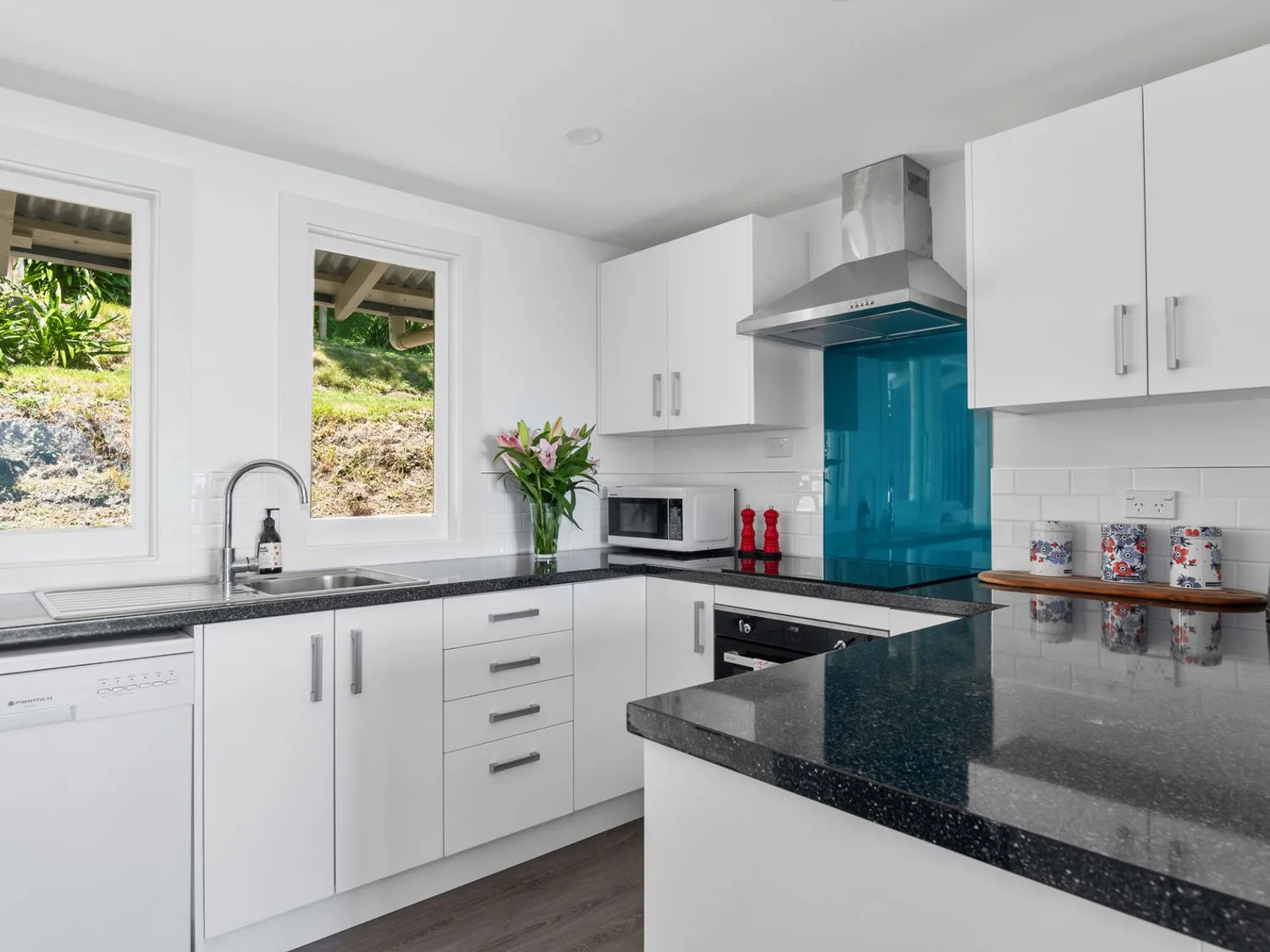 A kitchen with white cabinets black countertops a microwave flowers and a stainless steel oven at Bayview Bungalow - Nelson Holiday Home in Nelson