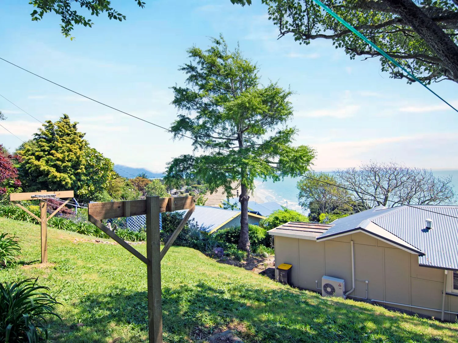 Un jardín trasero con césped, tendederos, árboles y vistas parciales a casas y al océano en Bayview Bungalow - Nelson Holiday Home, en Nelson.
