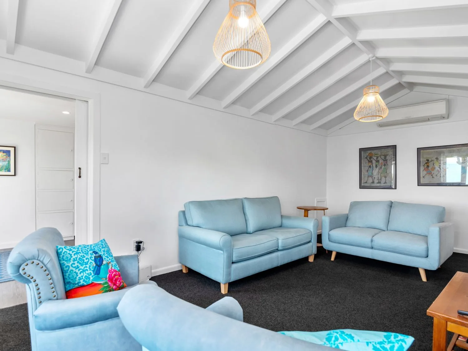Una sala de estar con sofás azules, un sillón azul y cuadros enmarcados en la pared en Bayview Bungalow Nelson Holiday Home, en Nelson.