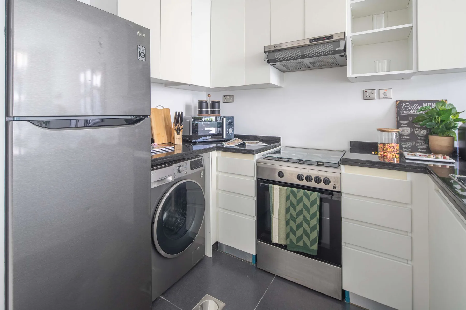 Una cocina compacta con armarios blancos, un refrigerador y una estufa.