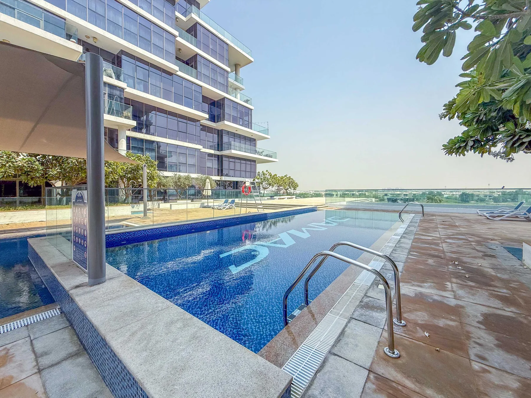 Una piscina junto a un edificio moderno, con asientos de descanso en la terraza.