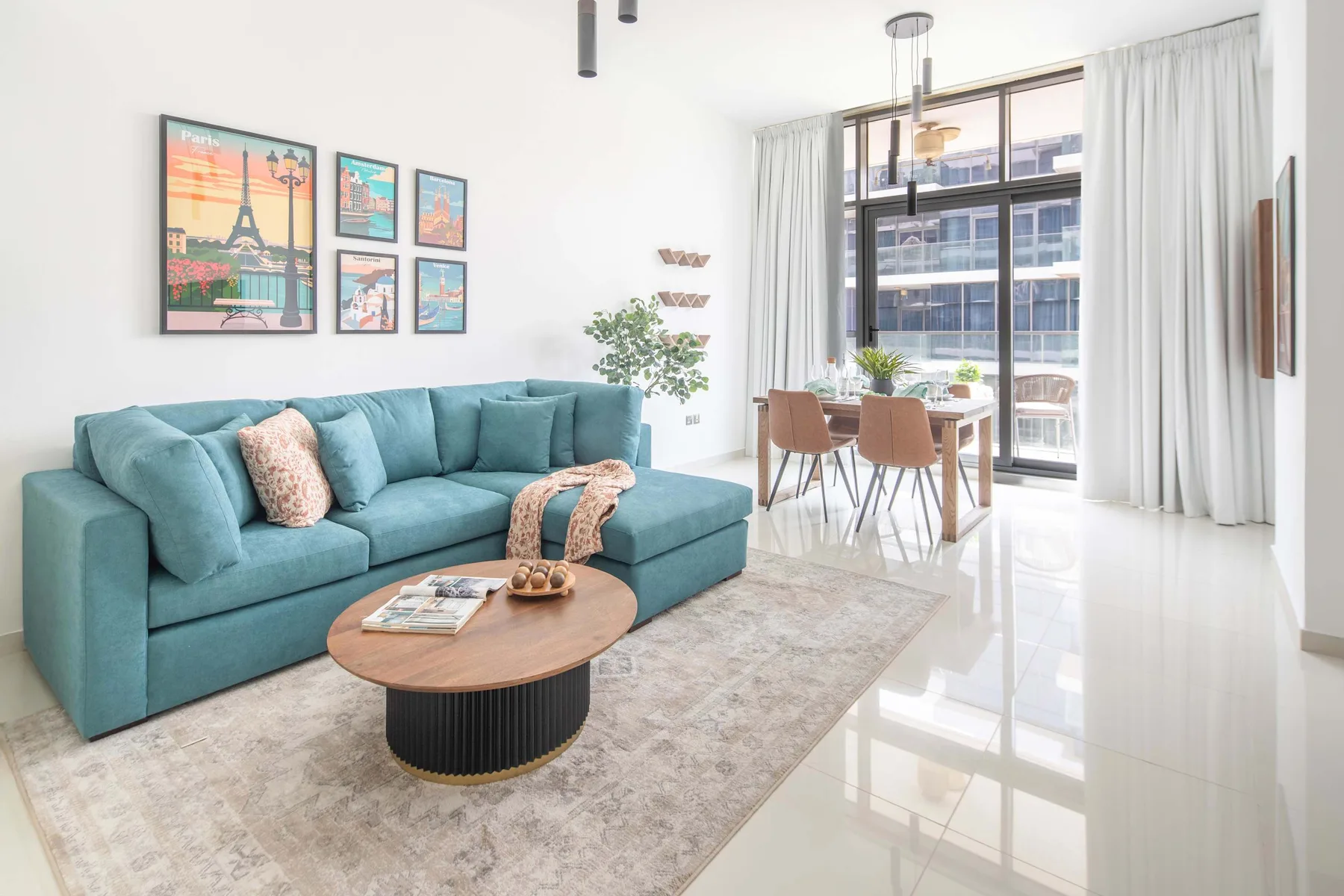 Una sala luminosa con asientos turquesa, una mesa de centro y un comedor junto a la ventana.
