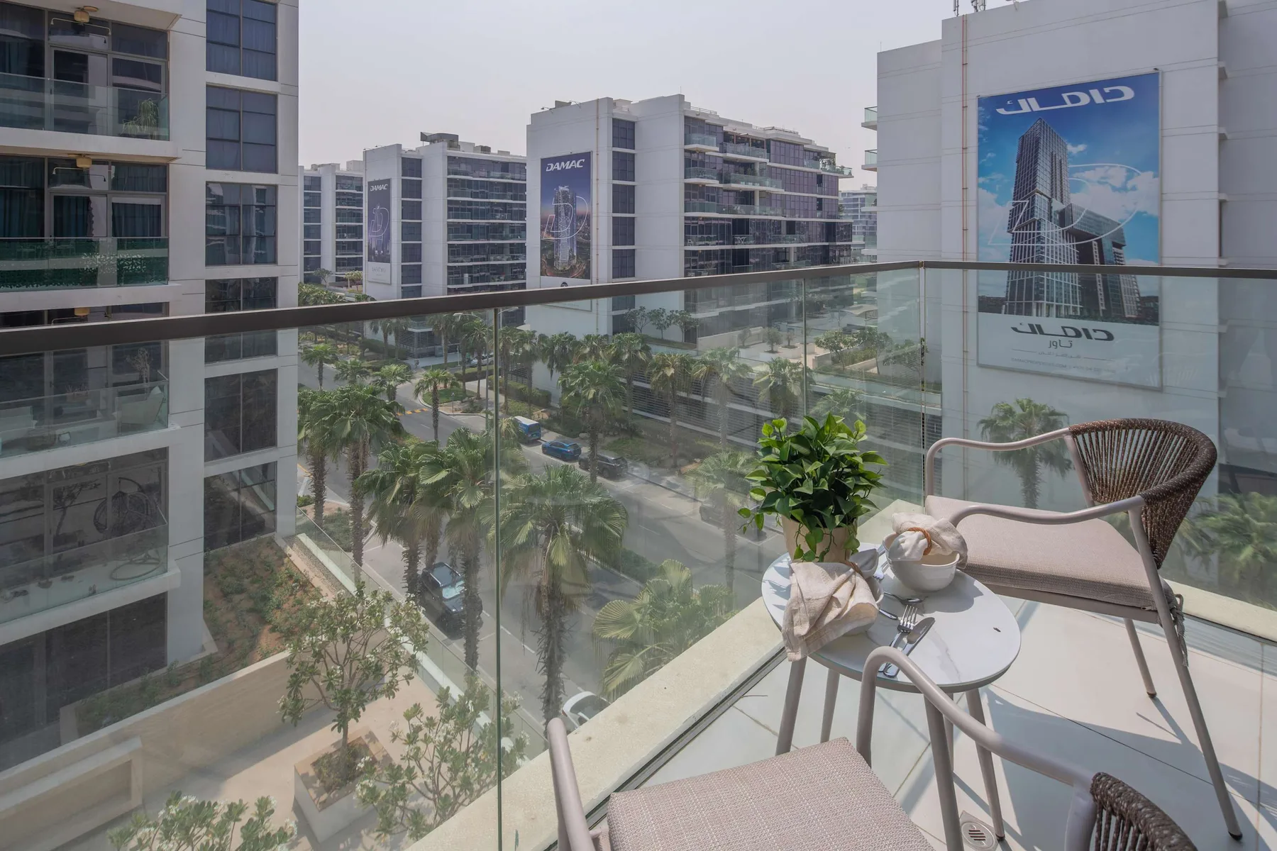 Una zona de estar en un balcón da a palmeras y edificios modernos.
