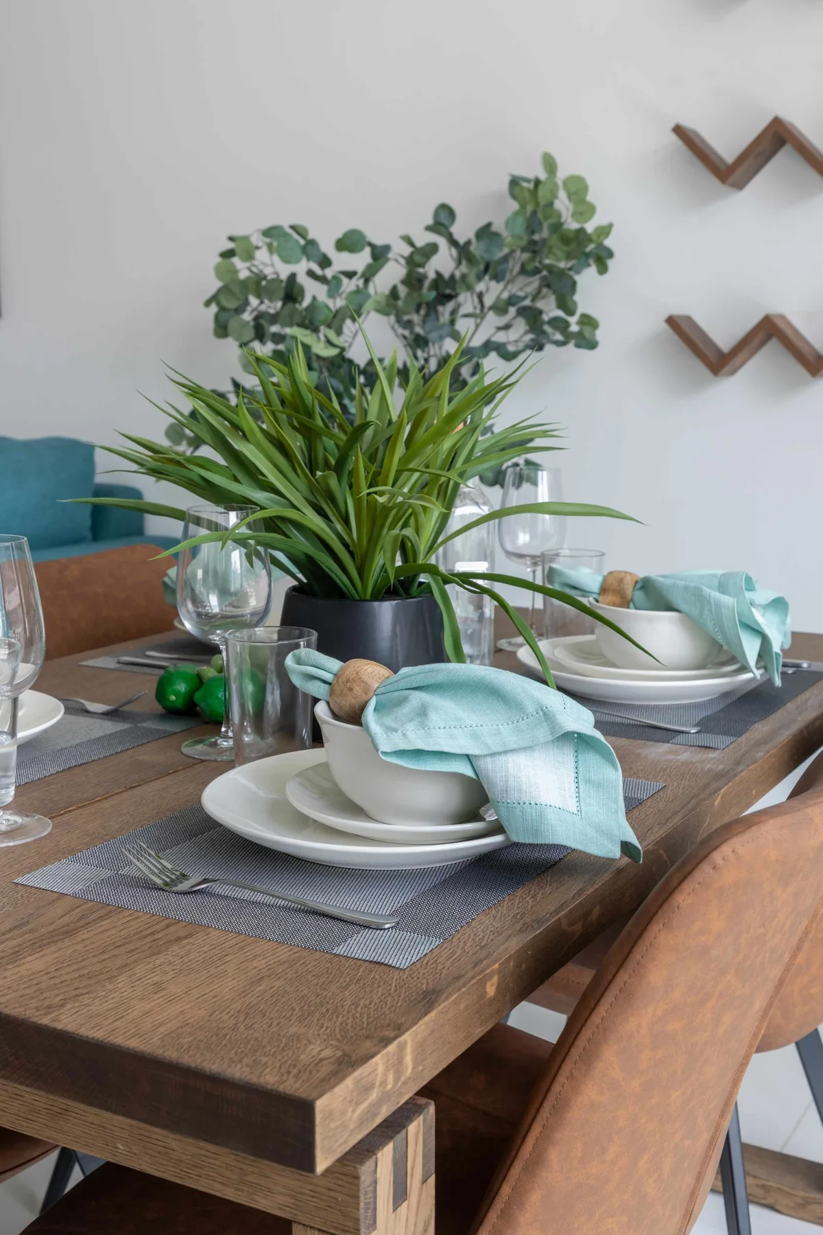 Una mesa de comedor está preparada con platos, copas y plantas verdes.