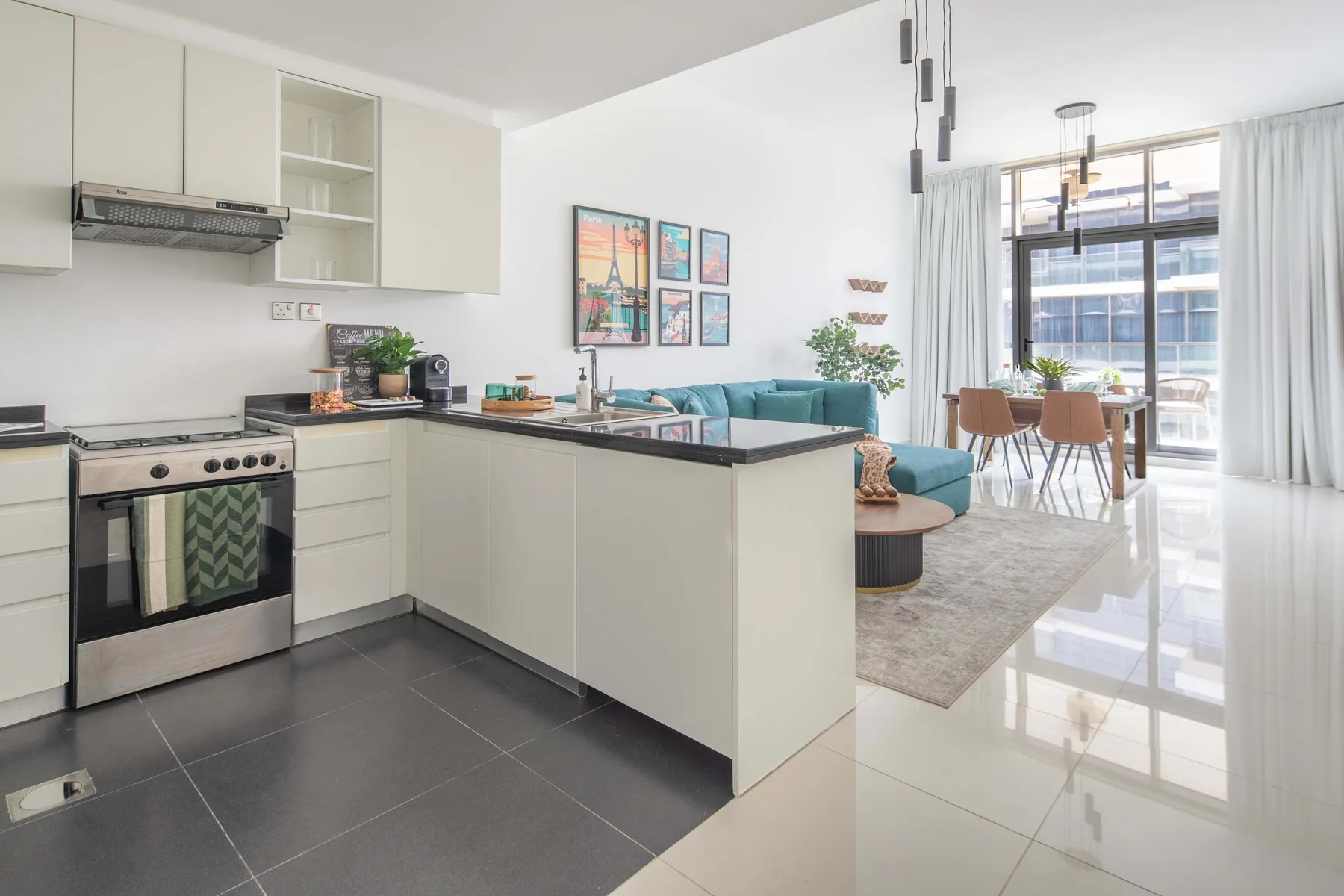 Una cocina y sala de estar diáfanas, con una mesa de comedor junto a grandes ventanas.