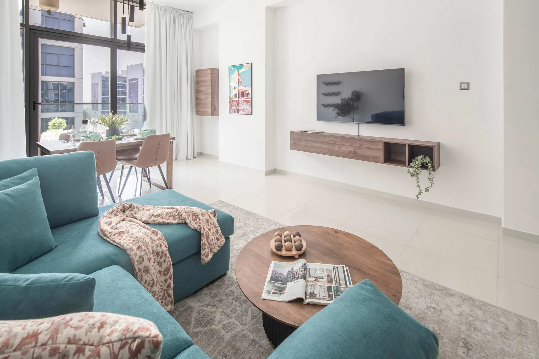 Una sala luminosa con asientos turquesa, una mesa de centro y un televisor en la pared.