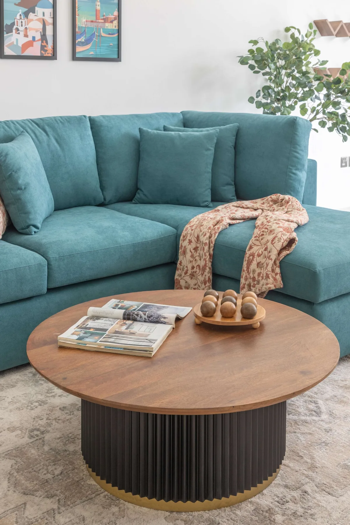 Una sala de estar con asientos color turquesa y una mesa de centro redonda de madera.