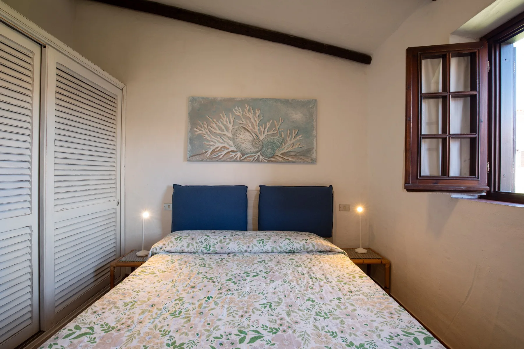 A bedroom with a double bed, floral bedding, and a painting above the headboard.