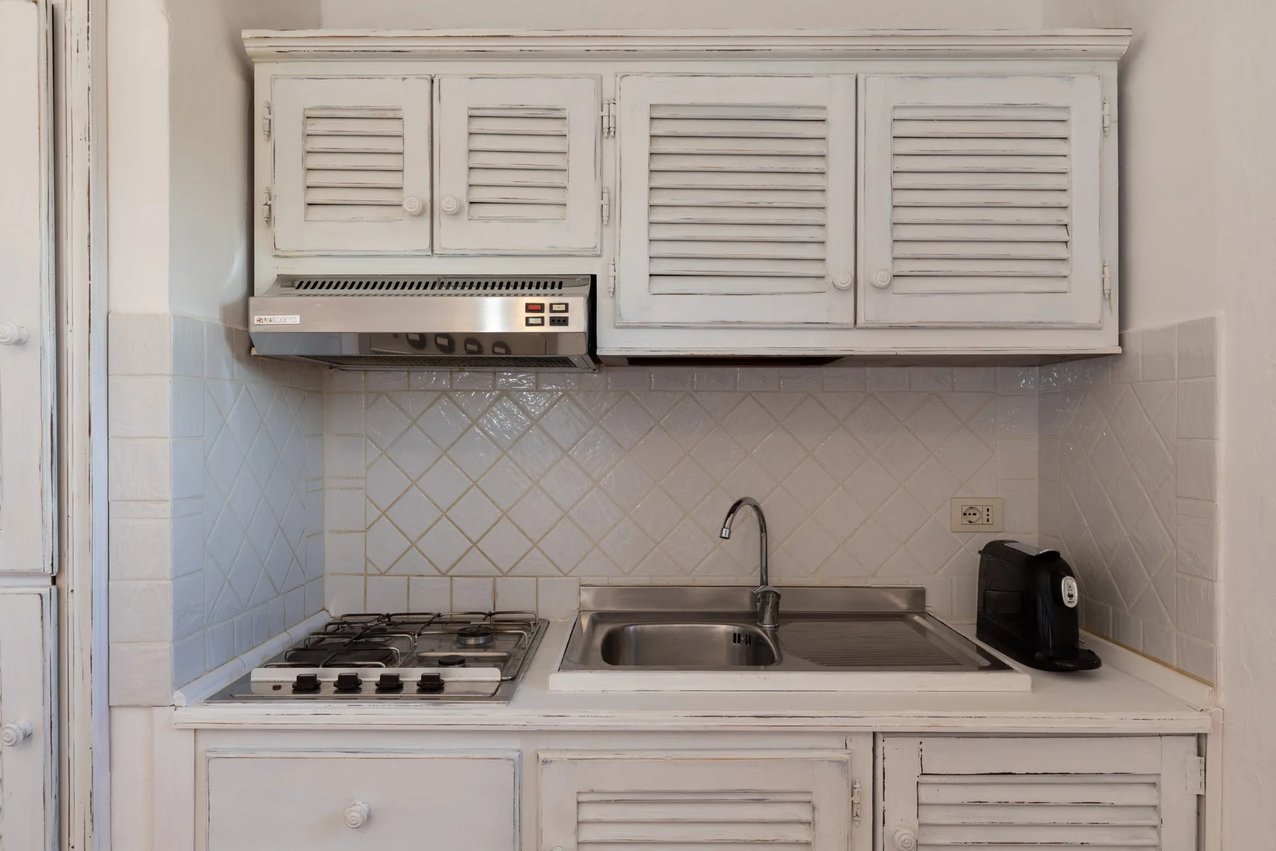 A compact kitchen has a stovetop, sink, and white cabinets.