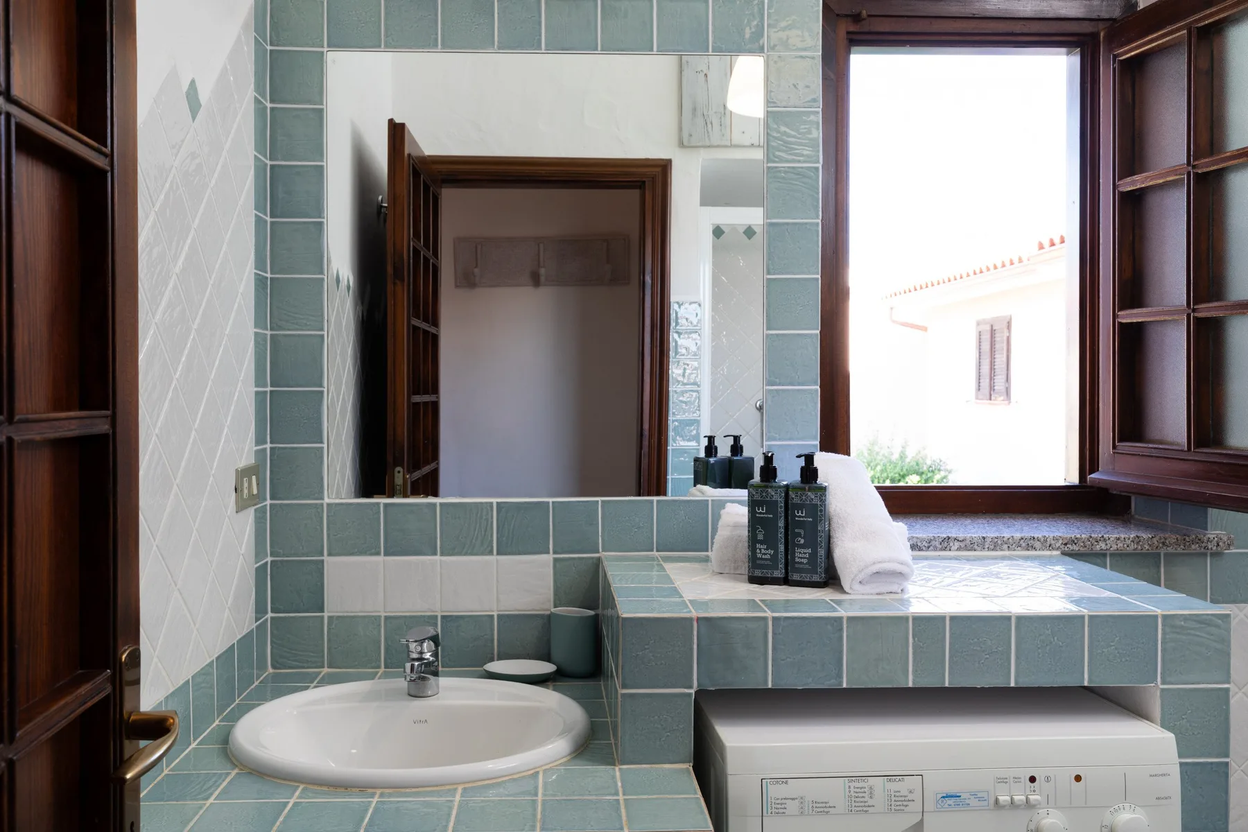 A tiled bathroom vanity with a sink, mirror, and open window.