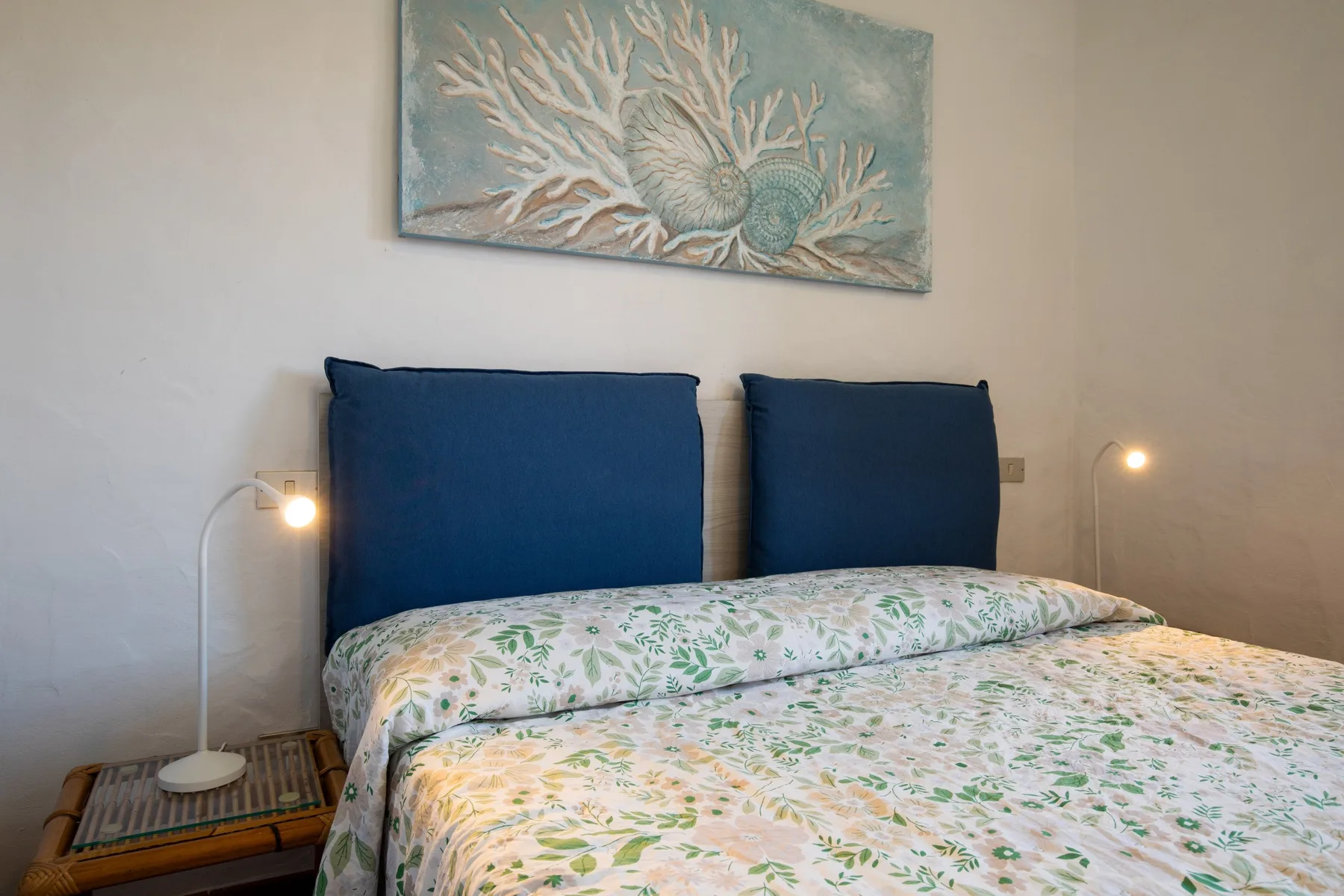 A bedroom with a bed dressed in green-and-white floral bedding and blue headboards.