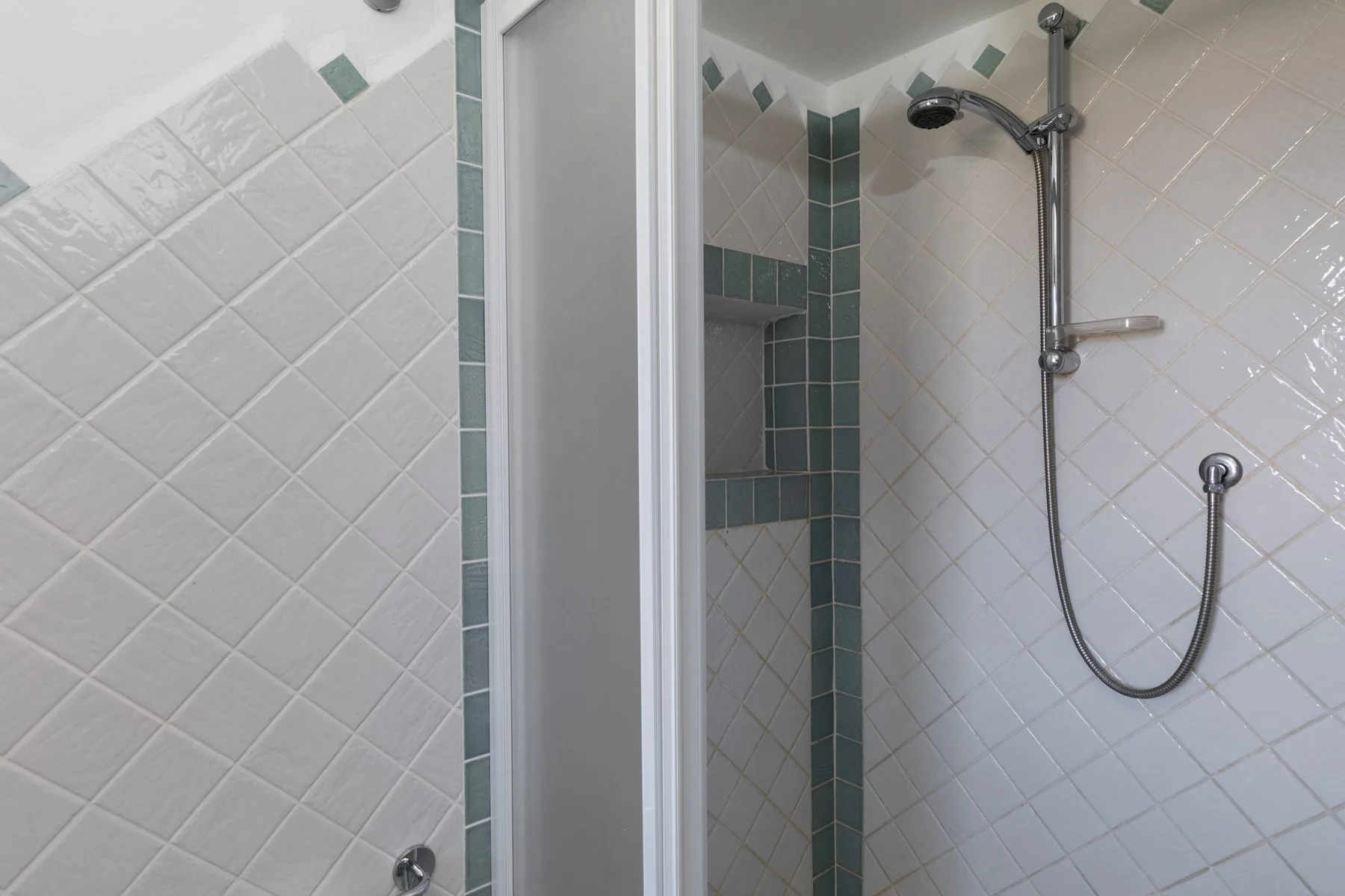 A tiled shower with a handheld showerhead and green accent tiles.