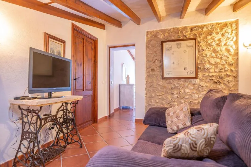 A living room with a television, seating, and exposed wooden ceiling beams.