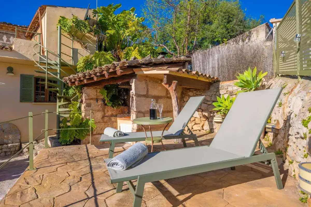 A stone patio features reclining seating beside a small rustic outdoor structure.