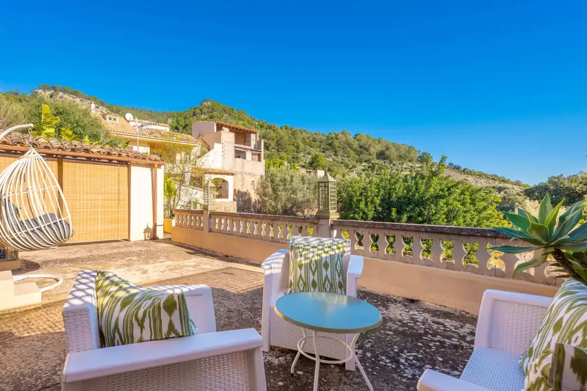 A sunny outdoor terrace with seating, a round table, and hillside views.