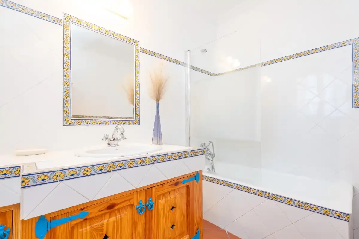 A tiled bathroom with a sink, mirror, and glass shower screen.