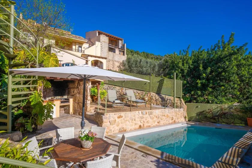 An outdoor pool beside a stone patio with shaded seating and greenery.