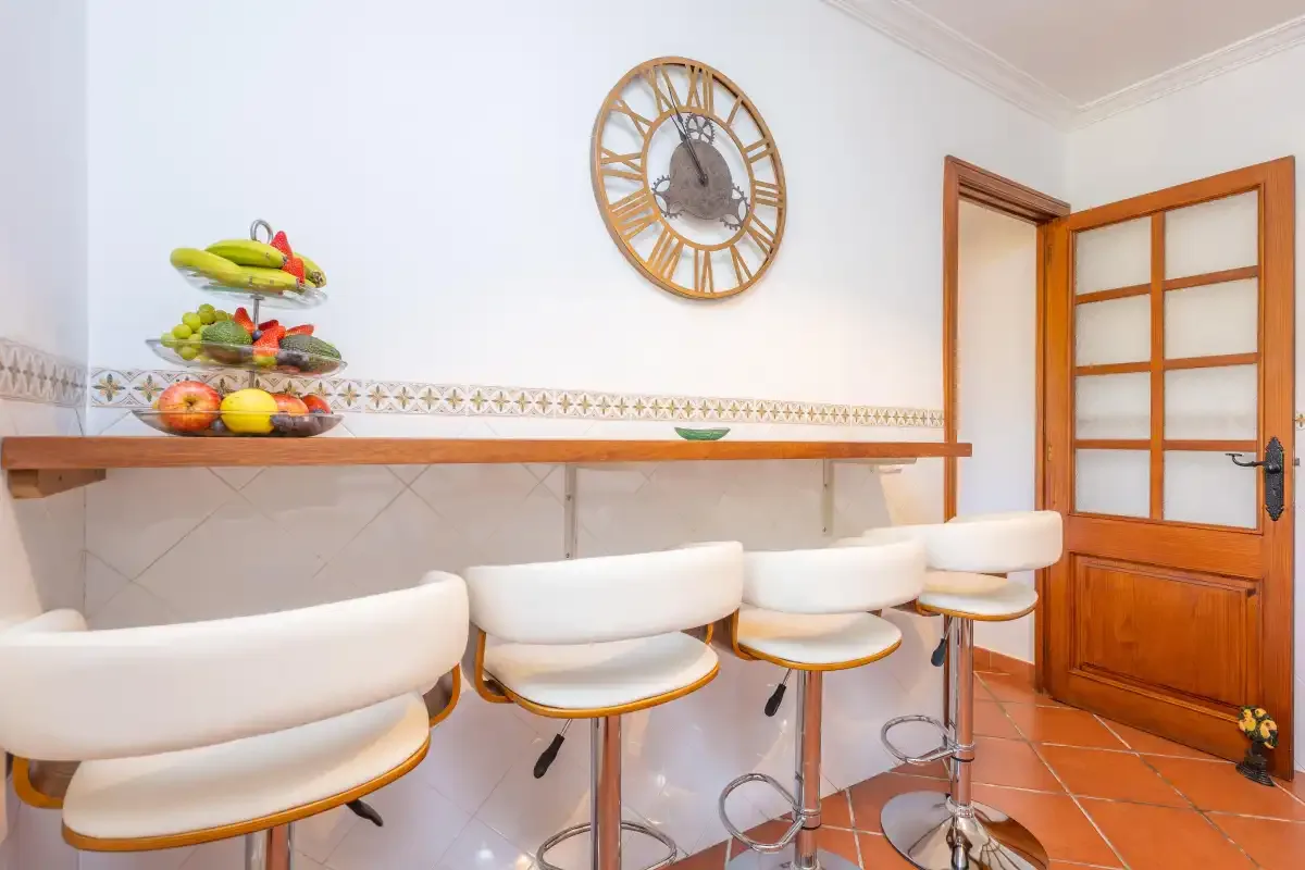 A kitchen counter with white seating, a fruit stand, and a wooden door.