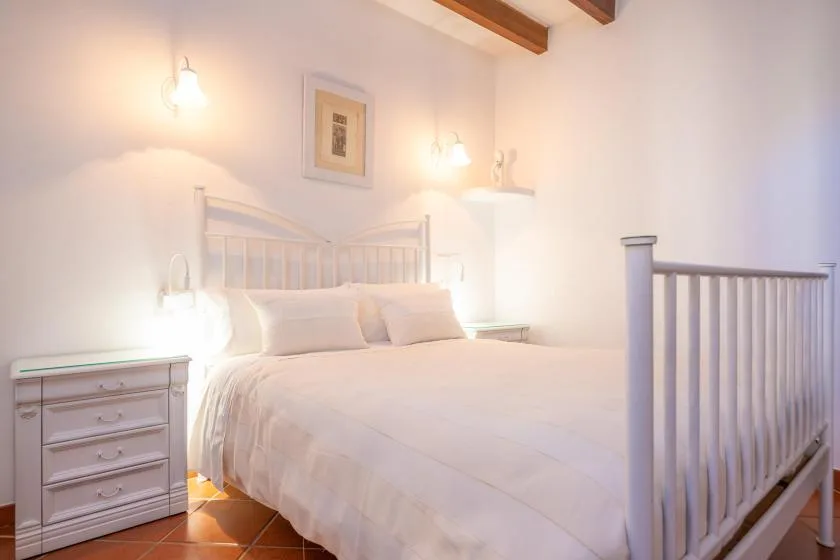 A bright bedroom with a white bed and wooden ceiling beams.