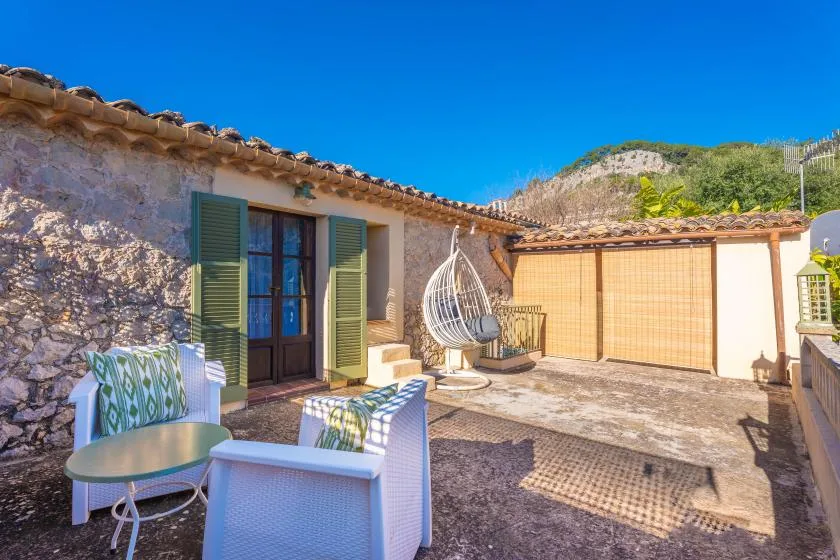 A stone patio with outdoor seating, a hanging chair, and a clear blue sky.